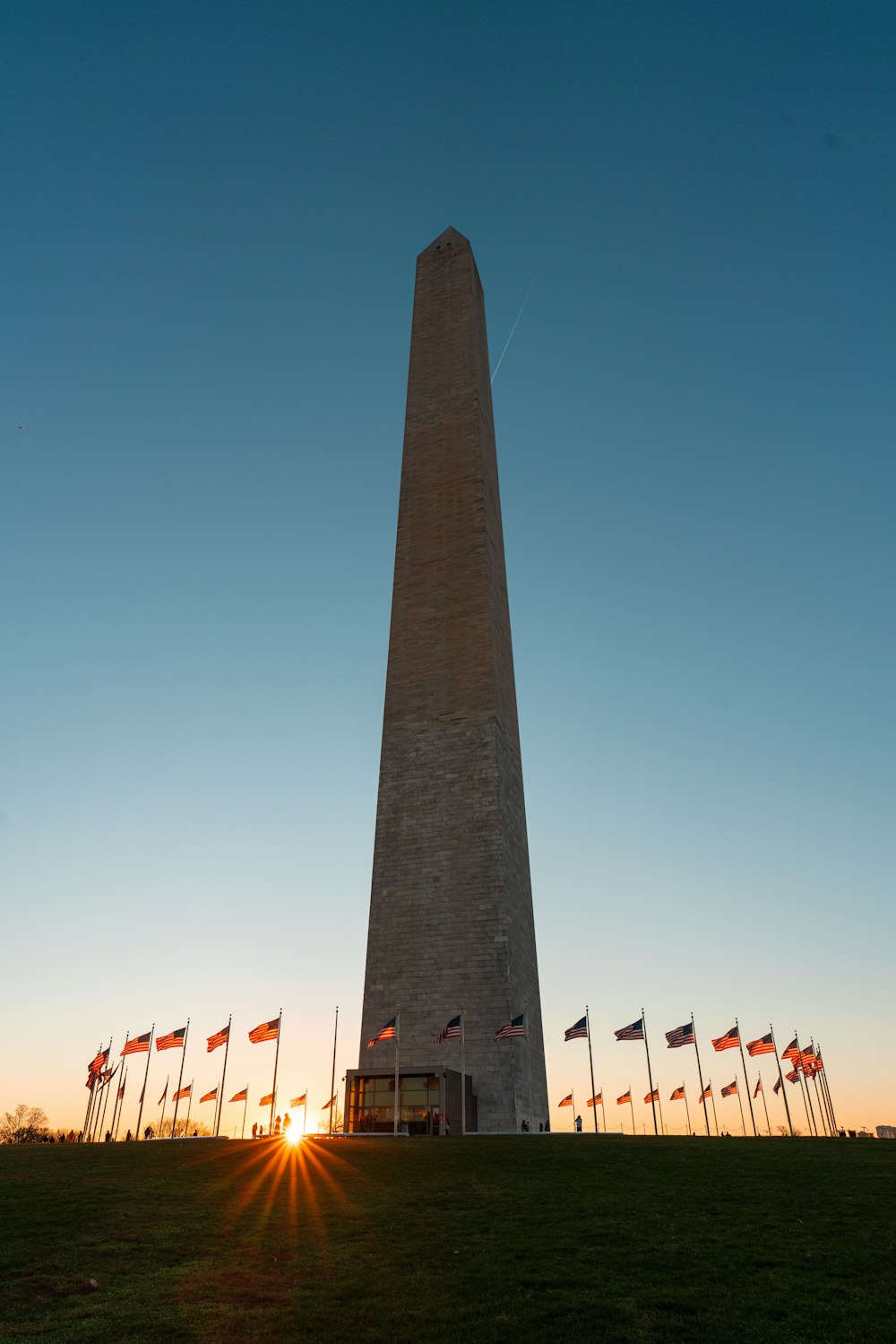 a tall monument with flags around it with Washington Monument in the background