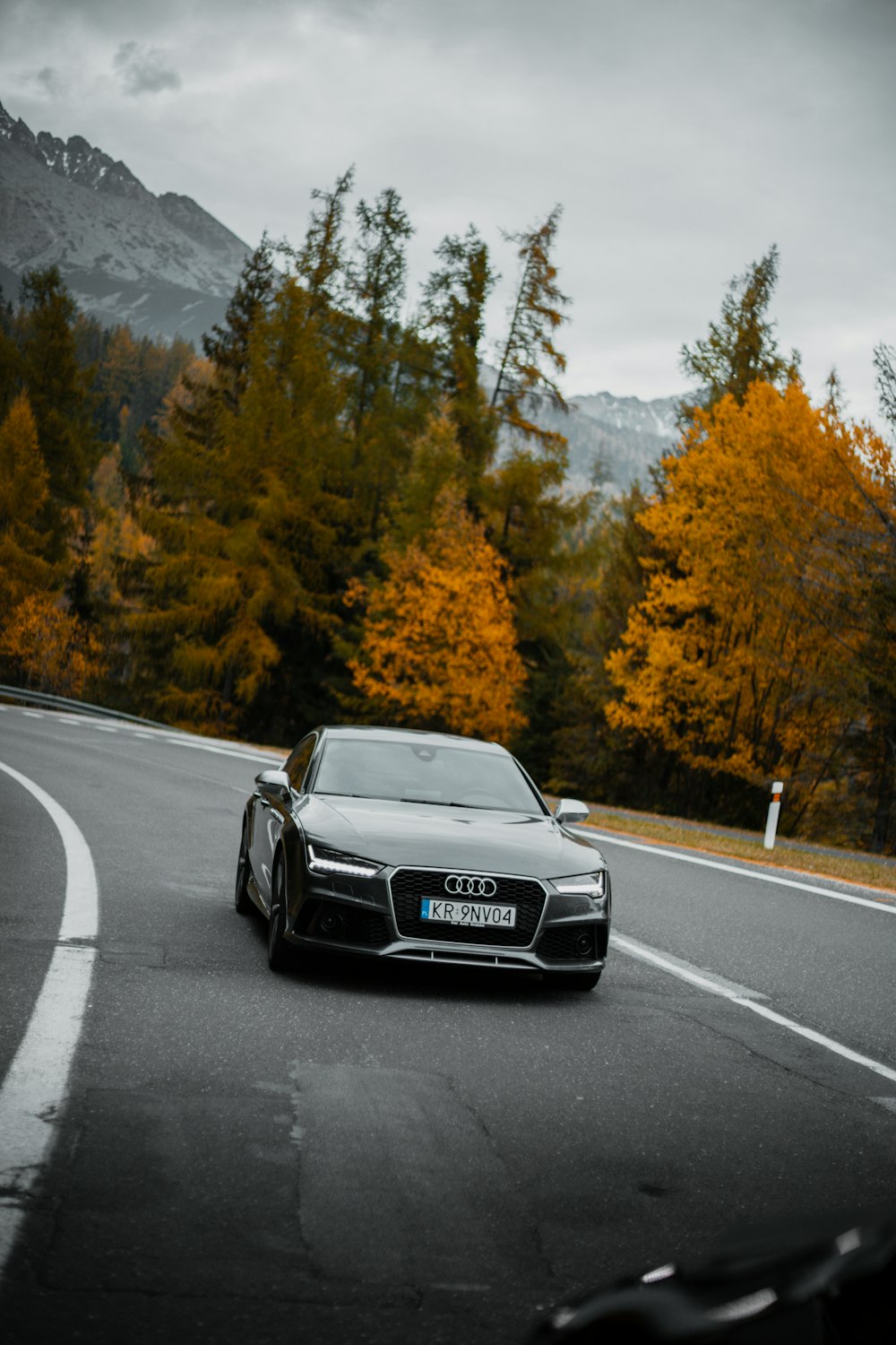 a black sports car driving on a road with trees and mountains in the background