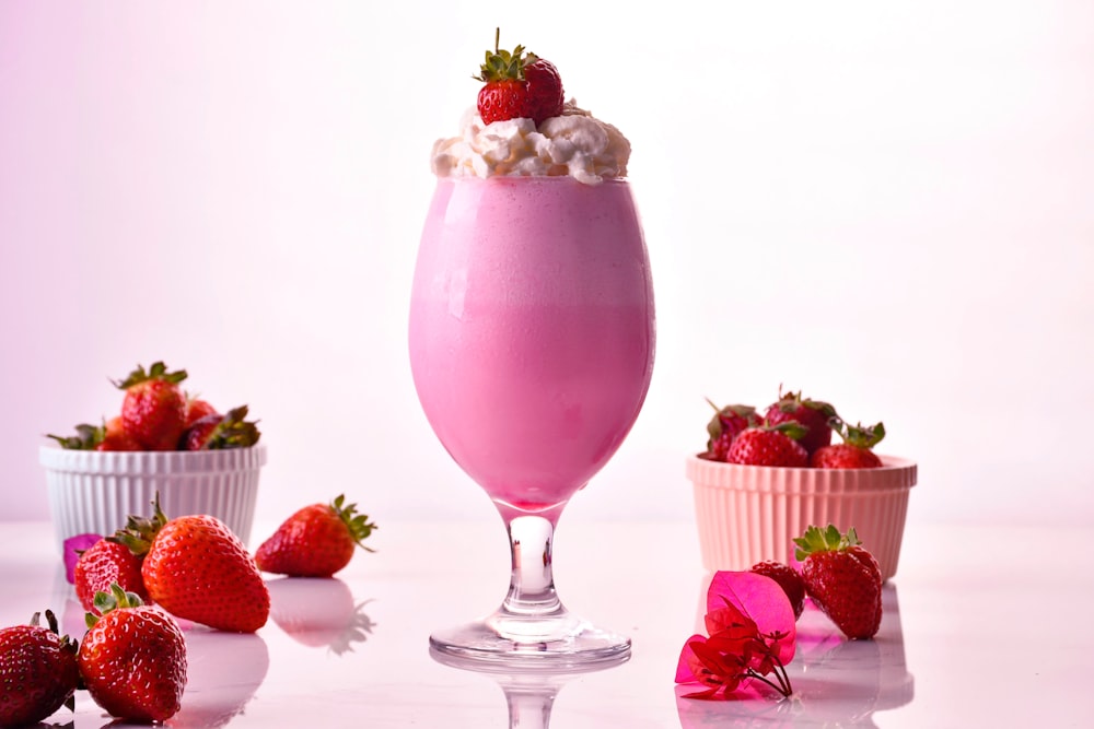 a glass of pink liquid with strawberries and a bowl of strawberries