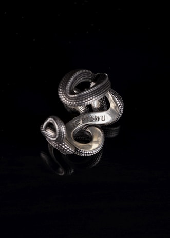 Close-up of a sleek silver ring on a dark textured surface, highlighting its minimalist design.