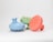 Three round scalp massagers with handle, featuring spiked bristles and made of plastic material. They are positioned side by side on a plain white background. Each massager is a different color: blue, green, and orange.