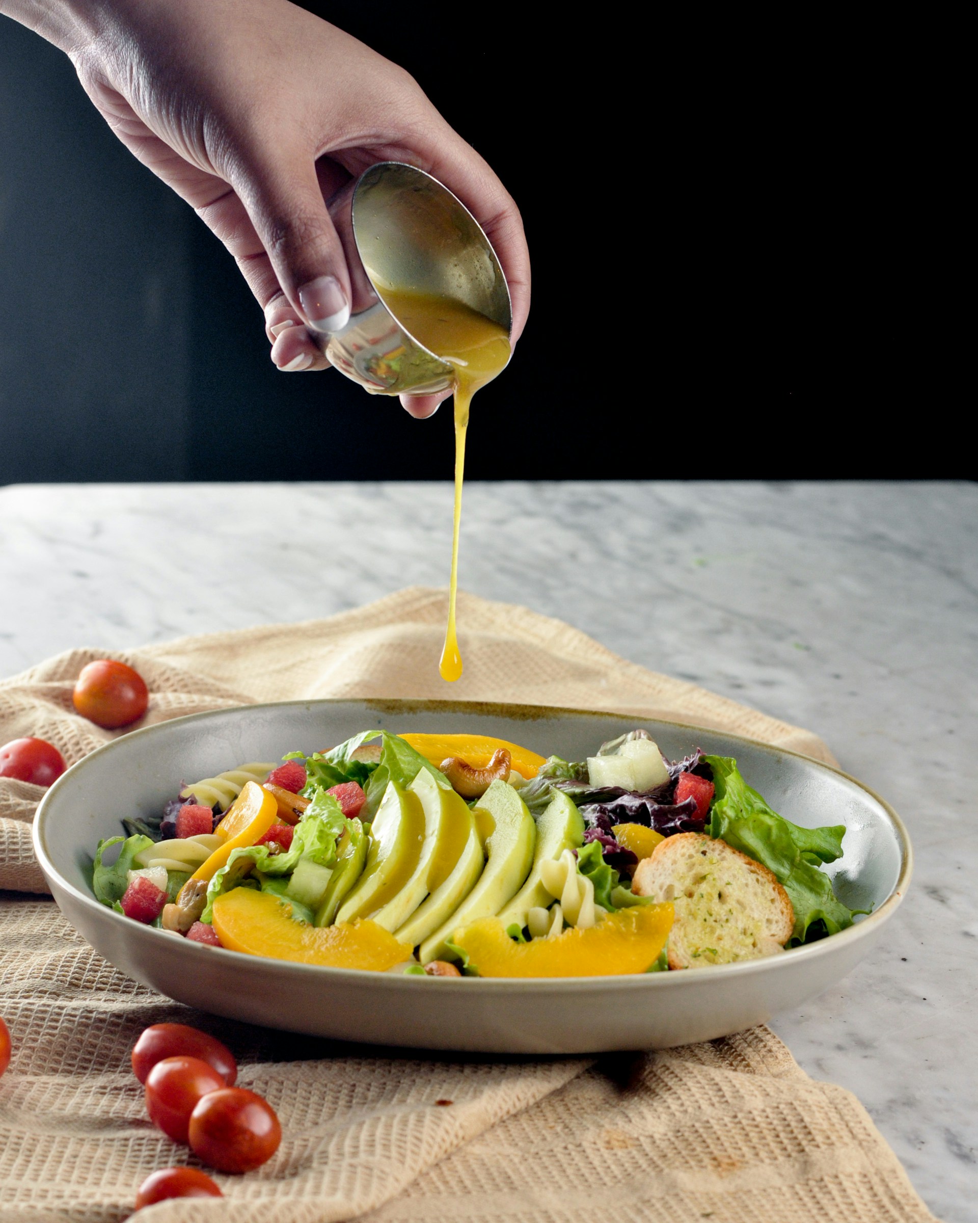 a hand pouring a glass of wine into a bowl of salad