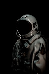 An astronaut suit is displayed prominently against a dark background. The suit is primarily silver with various technical details and fittings, including a helmet with a reflective visor. On the helmet, there are Cyrillic letters.