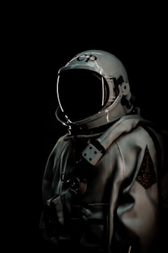 An astronaut suit is displayed prominently against a dark background. The suit is primarily silver with various technical details and fittings, including a helmet with a reflective visor. On the helmet, there are Cyrillic letters.