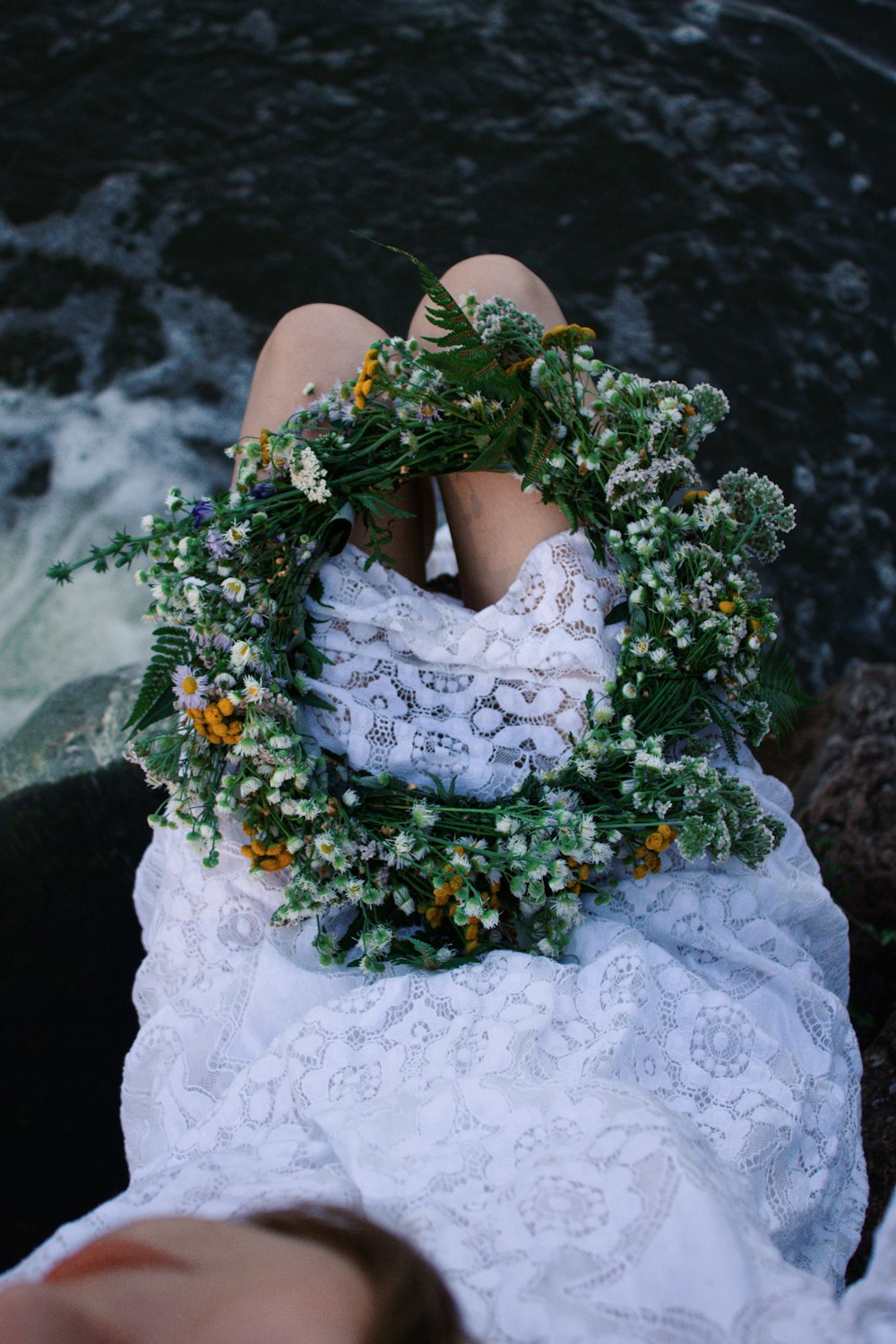 a person in a white dress with flowers on a rock