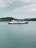 A large ferry with the phrase 'We Love Indonesia' painted on the side is sailing in calm waters. In the background, there is a hilly shoreline covered with greenery under a cloudy sky.