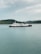 A large ferry with the phrase 'We Love Indonesia' painted on the side is sailing in calm waters. In the background, there is a hilly shoreline covered with greenery under a cloudy sky.