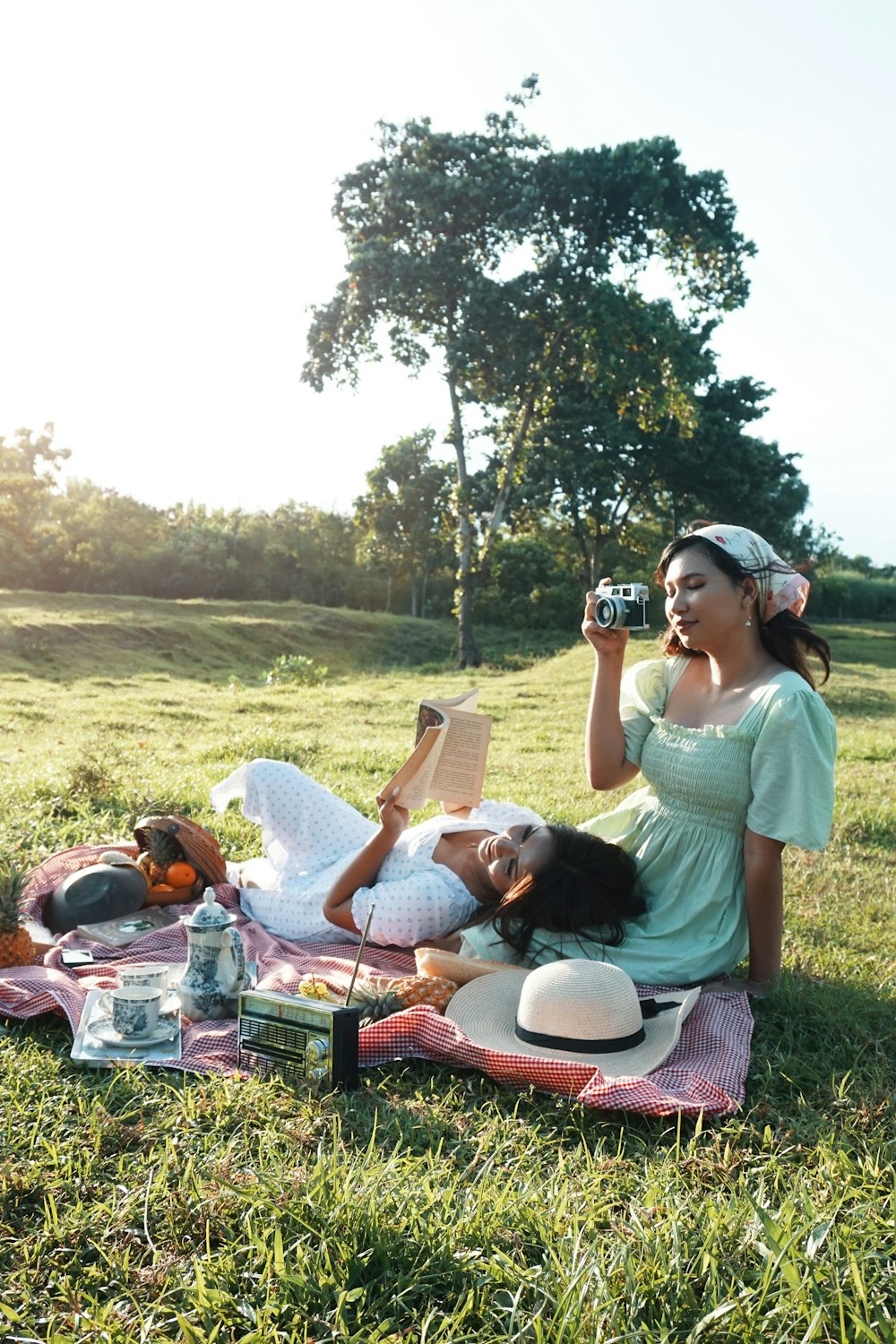 a woman taking a picture of a man lying on a blanket in a grassy field