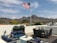 A rooftop patio with modern outdoor furniture and an American flag flying against a backdrop of mountains. The patio has blue cushioned chairs and small green plants in pots, with a table set that includes wicker chairs and decorative vases.