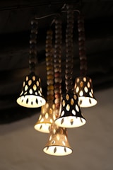 A cluster of ornate hanging lights with perforated shades, arranged in a descending pattern. The lights are suspended from bead-like chains and emit a warm, inviting glow.