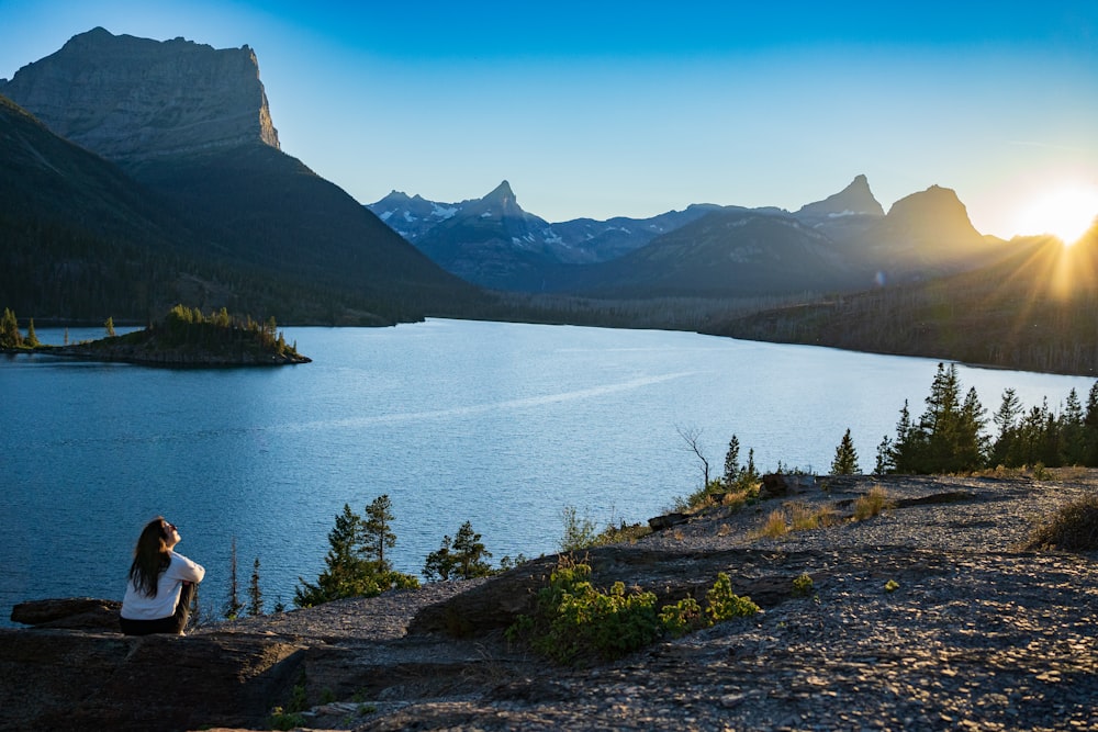 a person sitting on a rock by a body of water with mountains in the background