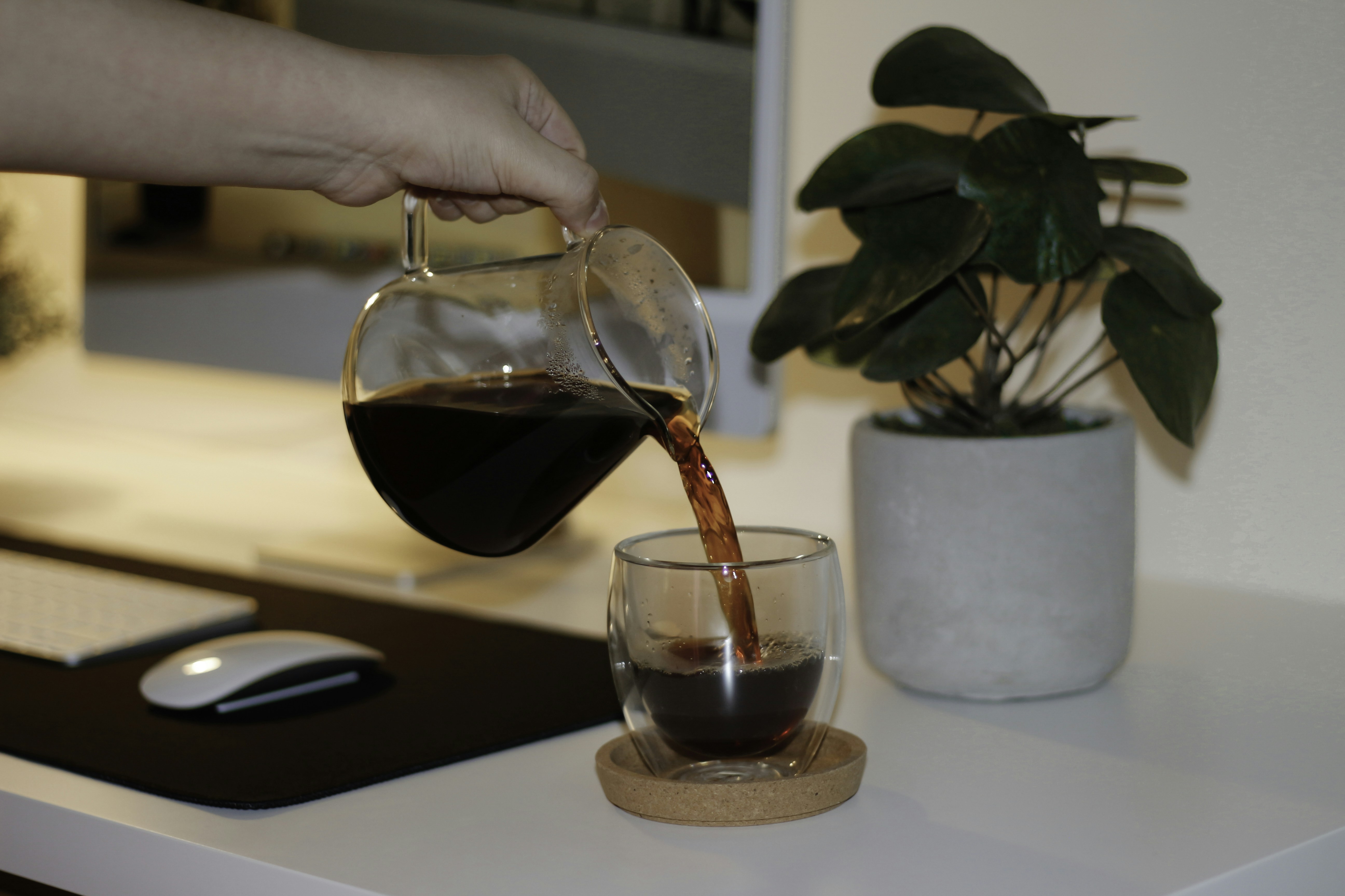 Coffee poured from a server into a glass beside a plant