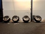 A row of freshly balanced car wheels lined up on the garage floor.
