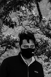 a man with a black and white face mask under a tree