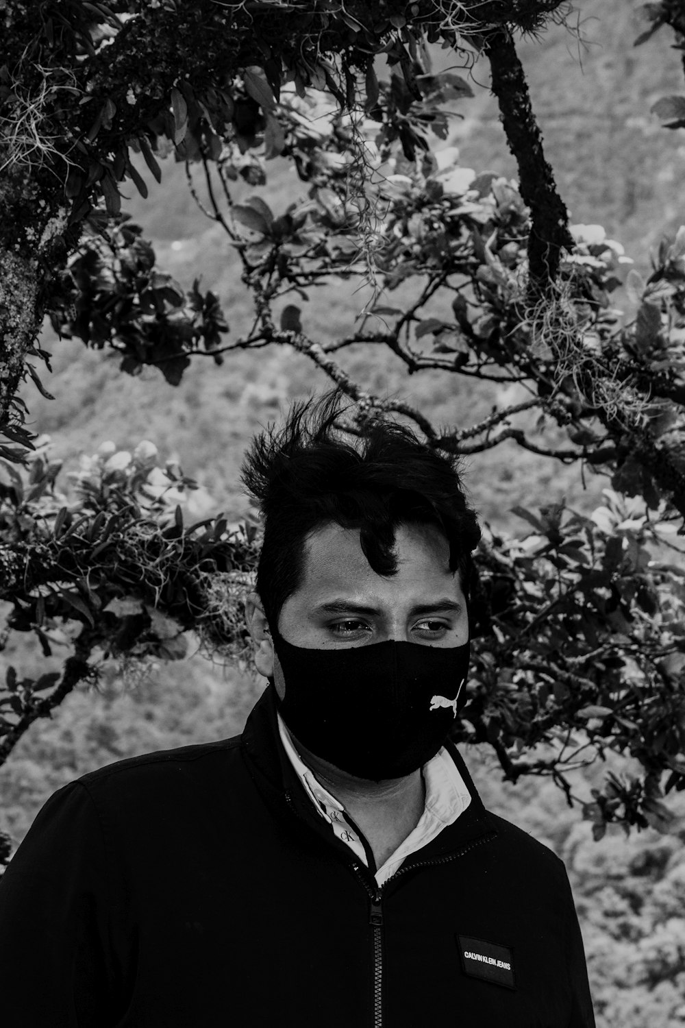 a man with a black and white face mask under a tree