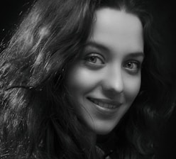 A black and white portrait of Tatiana Lebedianskaia holding her camera, smiling softly.
