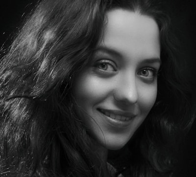 A black and white portrait of Tatiana Lebedianskaia holding her camera, smiling softly.