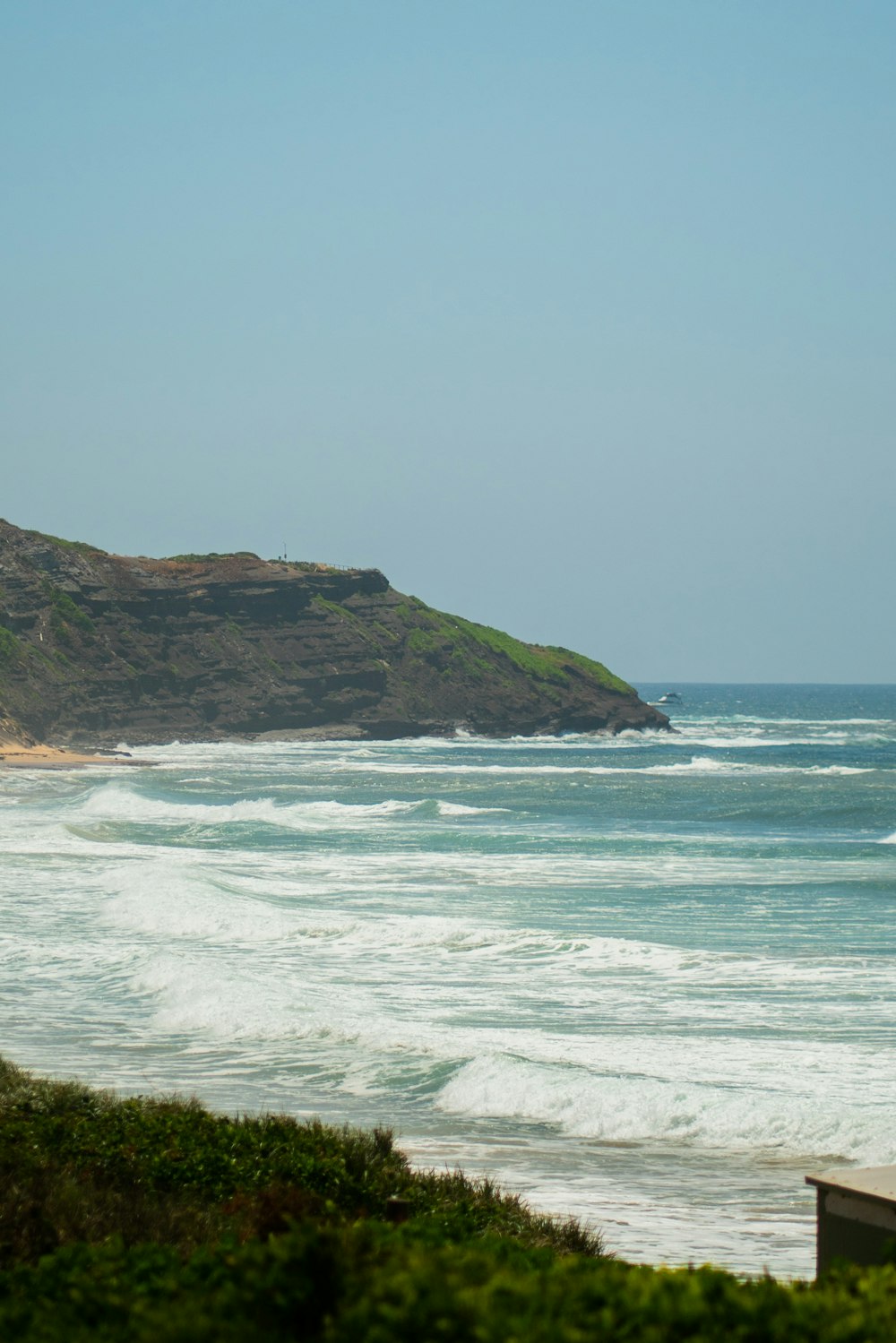 a beach with waves and a hill in the background
