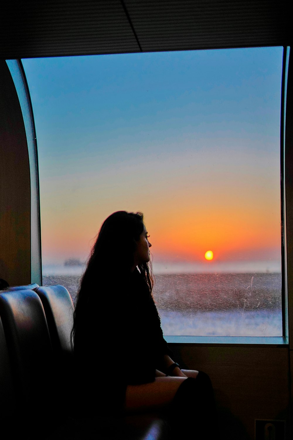 a person sitting on a couch looking out a window at the sunset