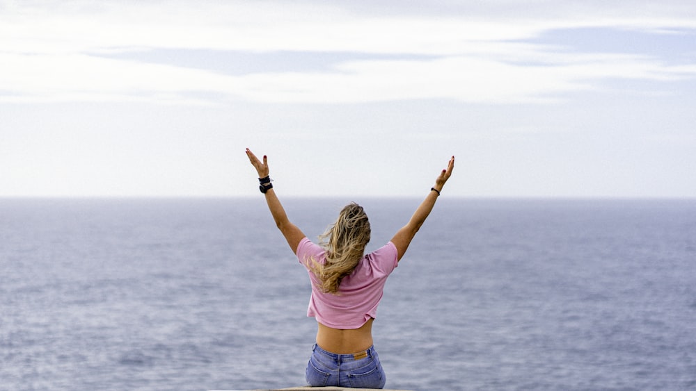 a woman with her arms raised in front of a body of water