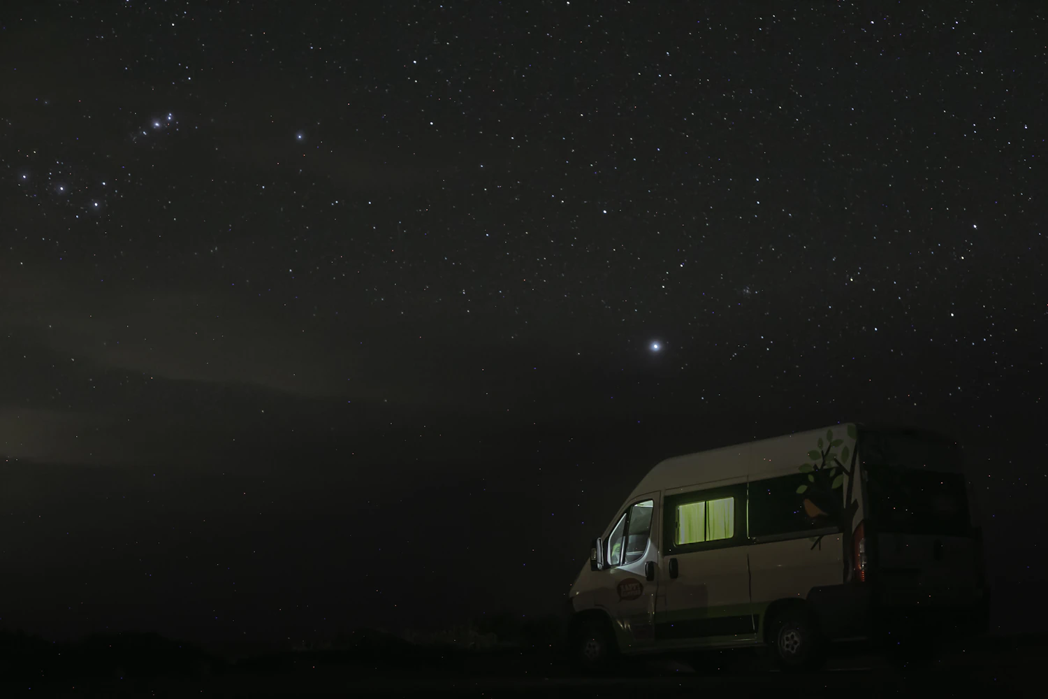 A touring van parked in a dark field with its interior light on