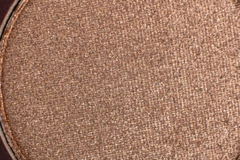 A close-up view of a textured, shimmering brown surface. The material appears to be finely powdered with a metallic sheen, suggesting it could be makeup or a similar product.