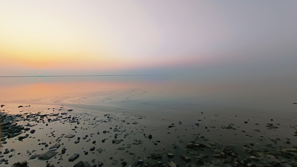 a large body of water with rocks and a sunset in the background