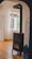 A cozy room with a traditional black wood stove stands against a white wall with blue artistic swirls. The room features wooden parquet flooring and white curtains that allow natural light through a set of tall windows.