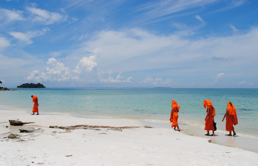 a group of people wearing orange clothes walking on a beach