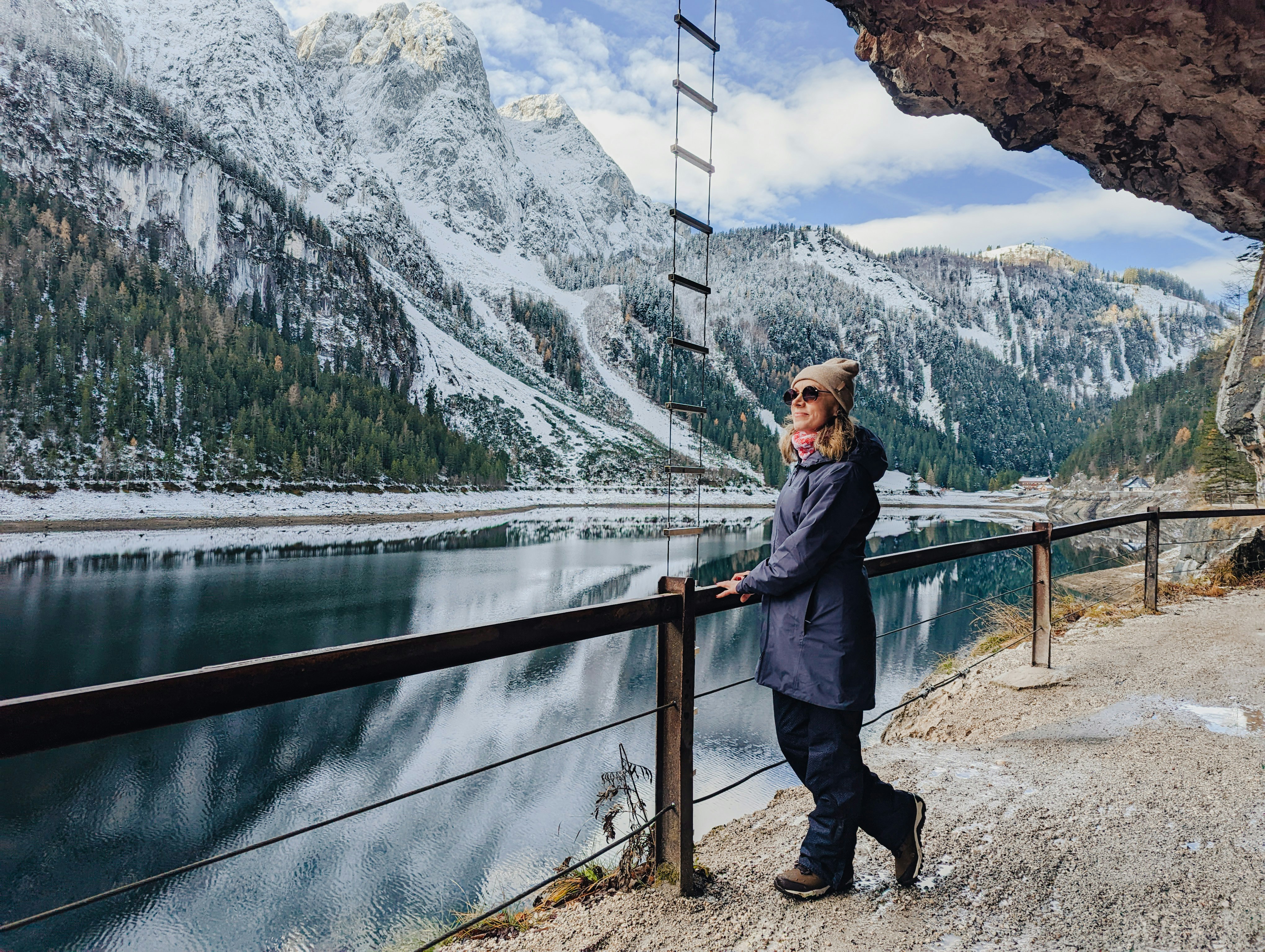 a man standing by a fence with a body of water and mountains in the background, Walking around Gosausee