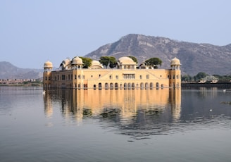 a large building with domed roofs by a body of water with Jal Mahal in the background