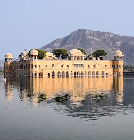 a large building with domed roofs by a body of water with Jal Mahal in the background