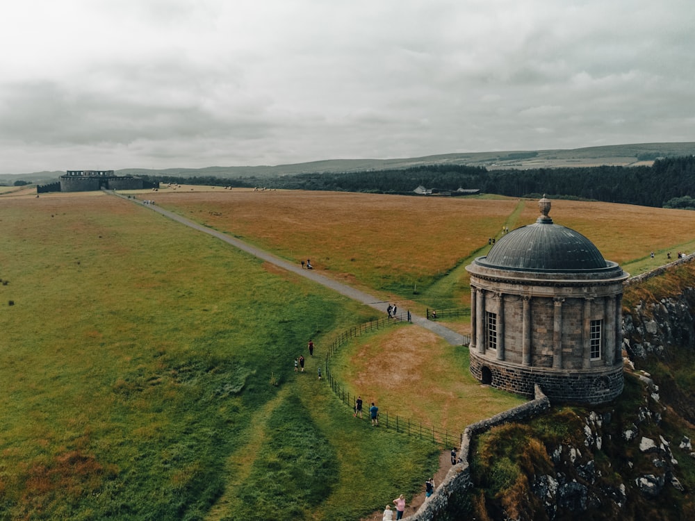 a stone building with a dome on a hill with a road and trees