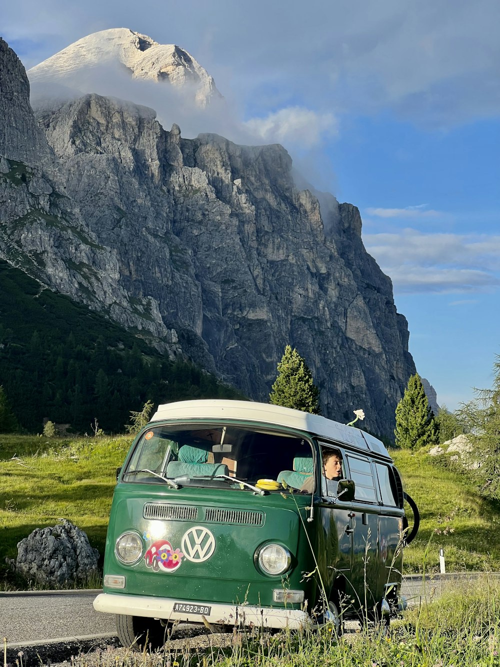 a green car on a road with mountains in the background
