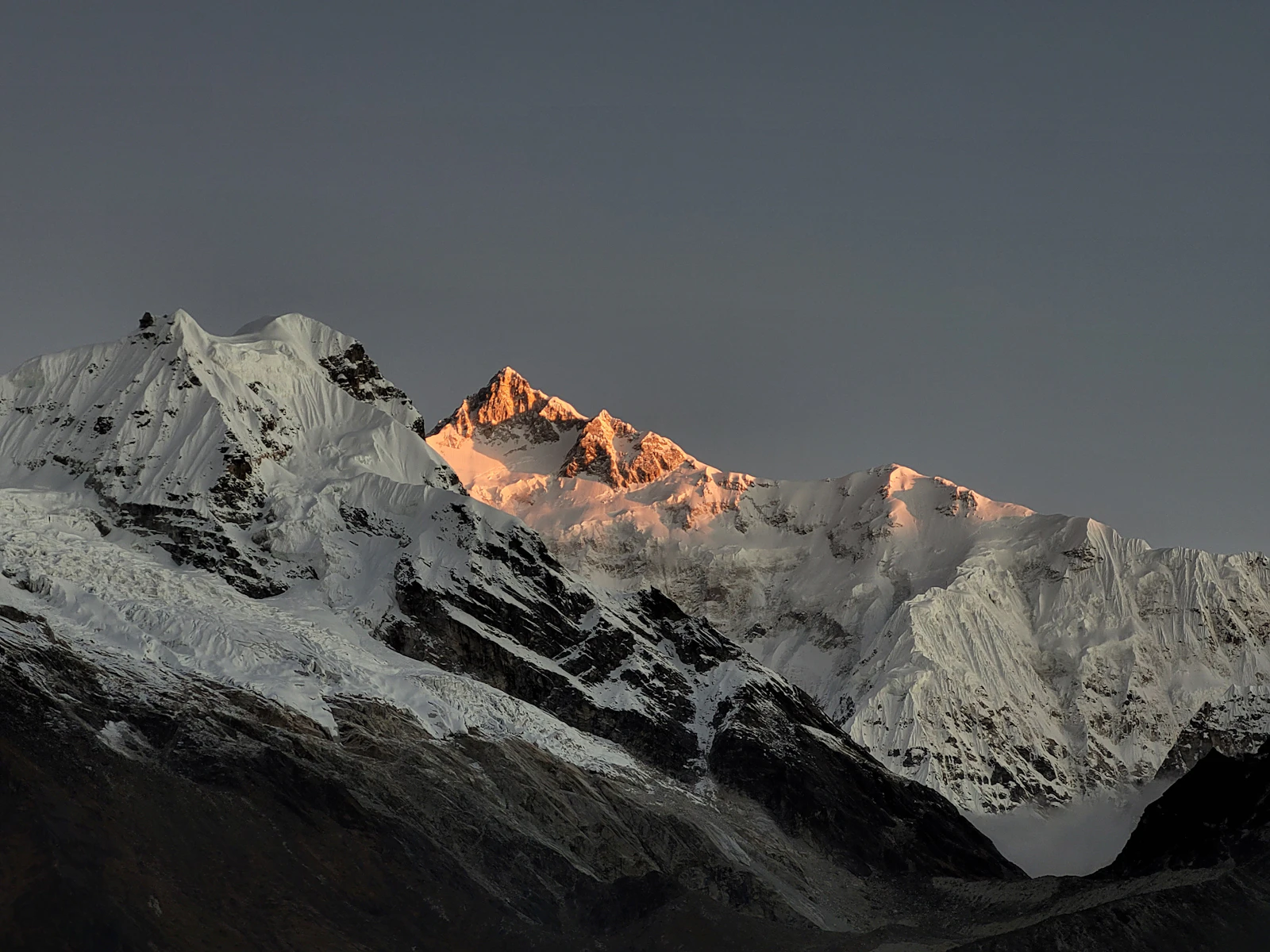 First light striking the summit of Kanchenjunga above its glaciers while the snow peak beside it stays in cold shadow