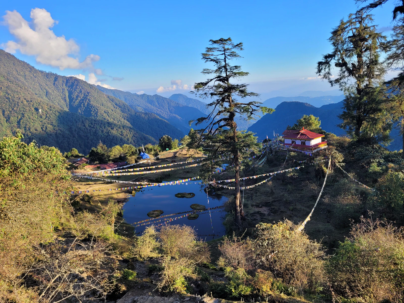 The small red roofed monastery above the prayer flag strung pond at Tshoka, forested valleys of West Sikkim falling away beyond