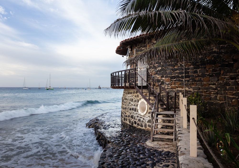 a stone wall with a staircase leading to a beach with boats in the water