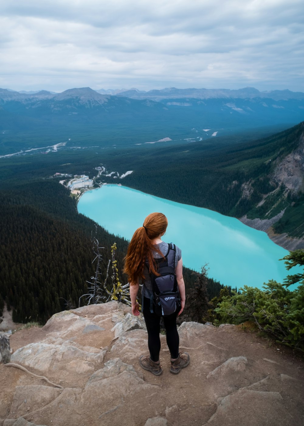 Una persona parada en una roca con vistas a un valle y un cuerpo de agua