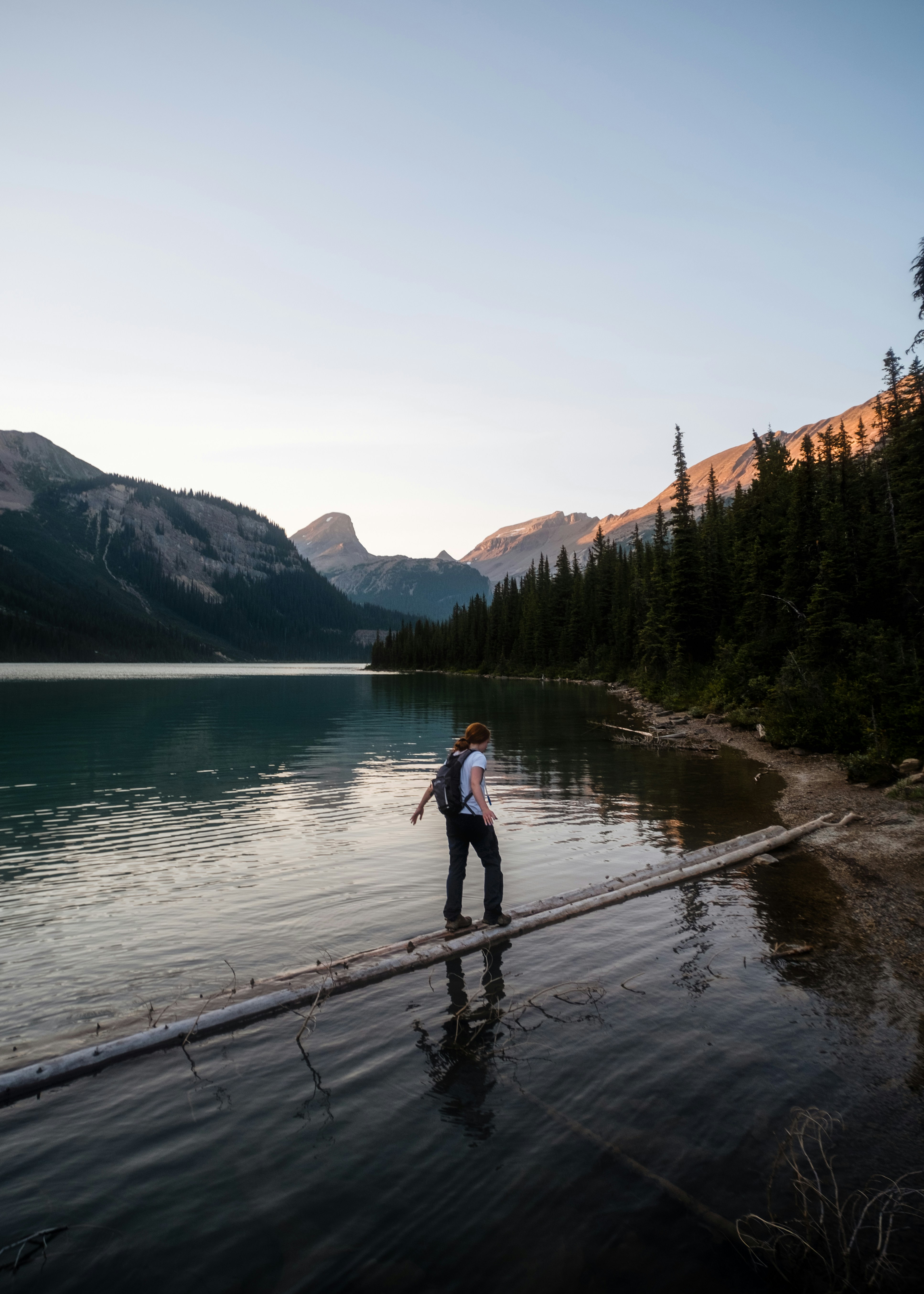 a man standing on a dock over a lake with mountains in the background