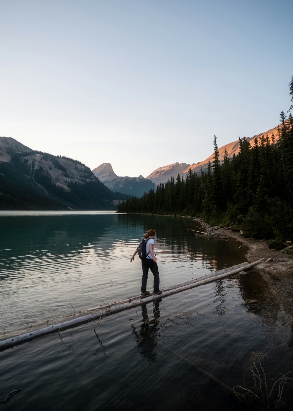 a man standing on a dock over a lake with mountains in the background