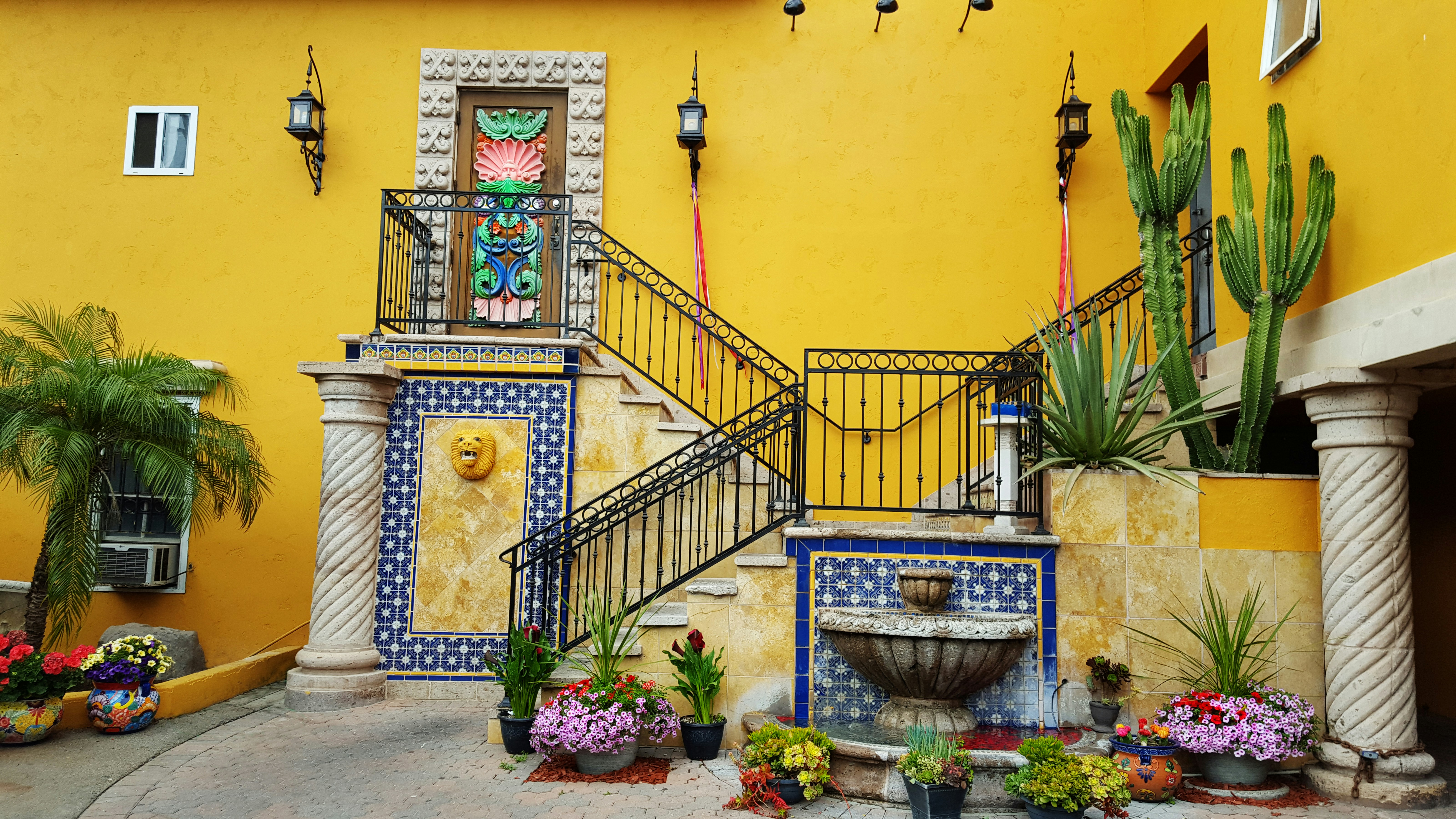 a yellow building with a fountain and plants, 