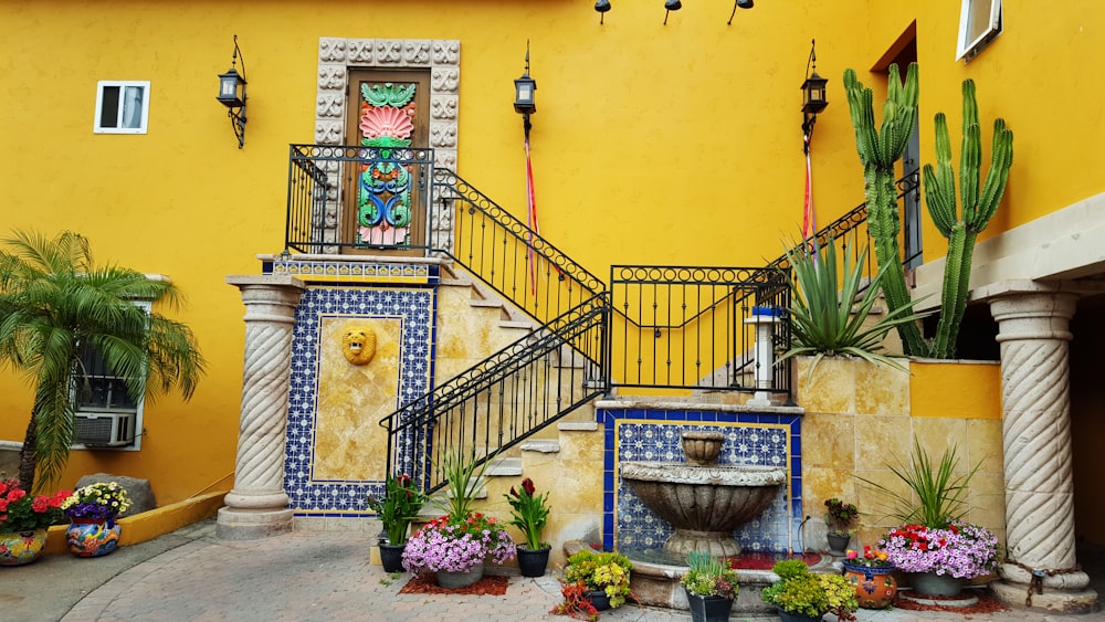 a yellow building with a fountain and plants