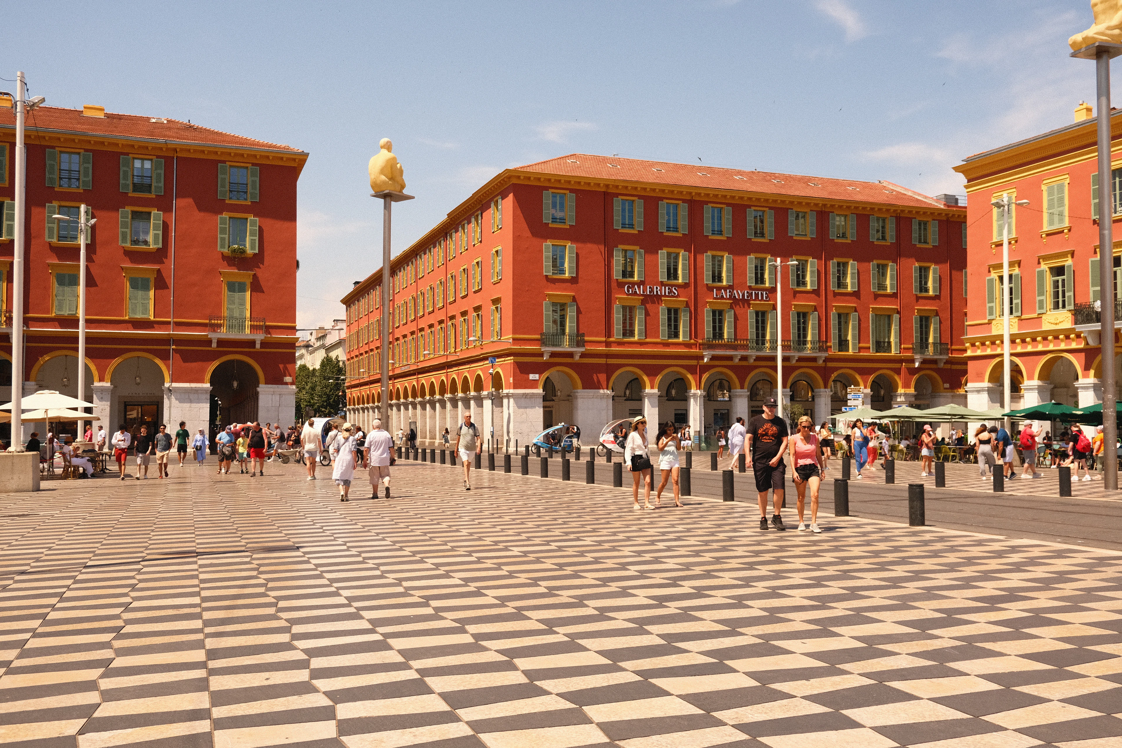 Place Massena in Nice, its black-and-white checkerboard paving spreading in front of the red-ochre arcaded buildings and the Galeries Lafayette storefront.