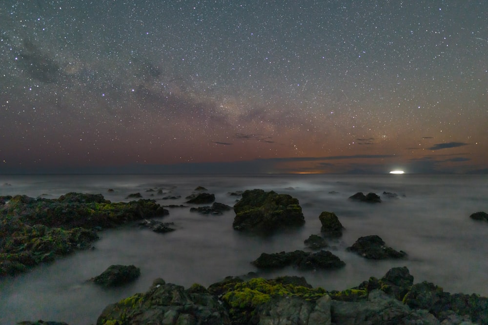 uma praia rochosa com um céu estrelado acima