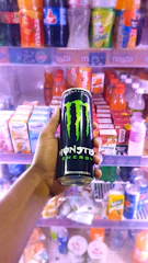 Close-up of cold energy drinks like Monster and Alani lined up inside a sleek vending machine.