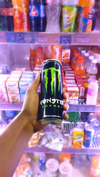 Close-up of cold energy drinks like Monster and Alani lined up inside a sleek vending machine.
