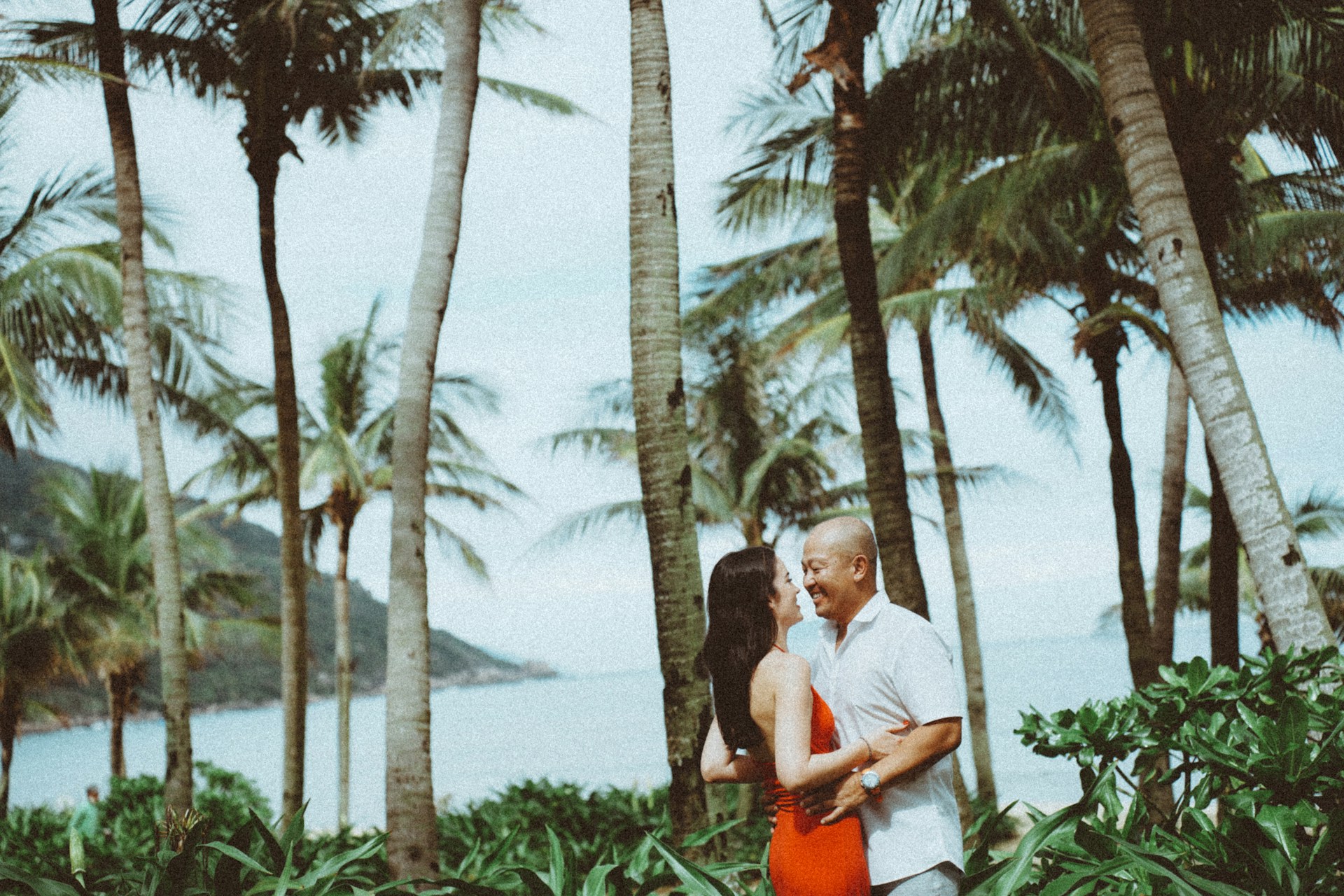 a man and woman standing next to palm trees and a body of water