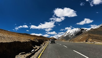 A winding mountain road in Spiti Valley under a bright blue sky with travelers enjoying a scenic drive.