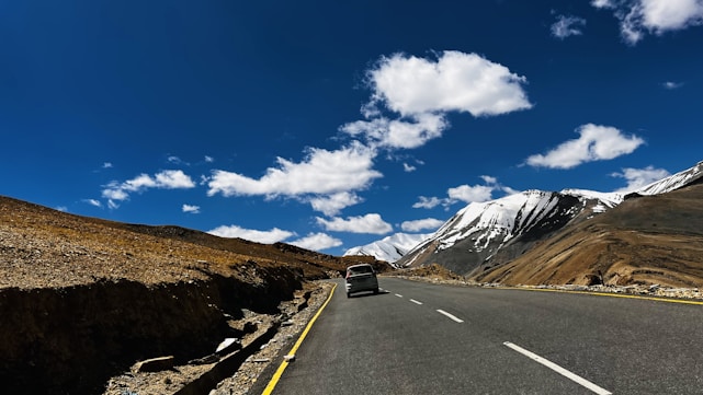 A winding mountain road in Spiti Valley under a bright blue sky with travelers enjoying a scenic drive.