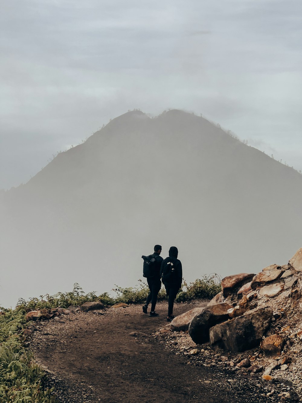 two people standing on a dirt path with a mountain in the background